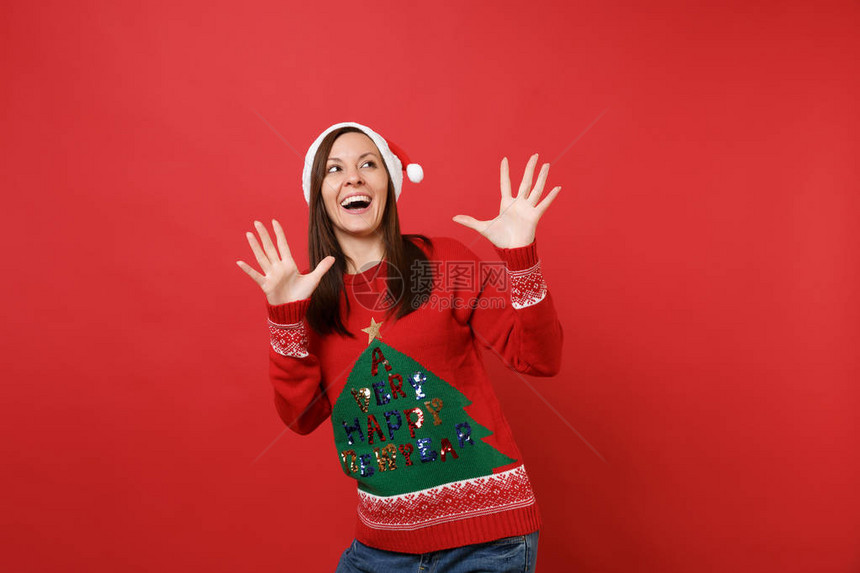 快乐的年轻女孩在针织毛衣圣诞帽抬头伸展双手指孤立在红色背景新年快乐2019庆祝节日派对理念图片