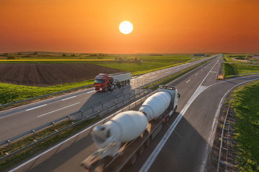 两辆用于不同目的卡车朝着太阳行驶在美丽的日落高速公路上的快速模糊运动图像塞尔维亚贝尔格莱德附近高速公路图片