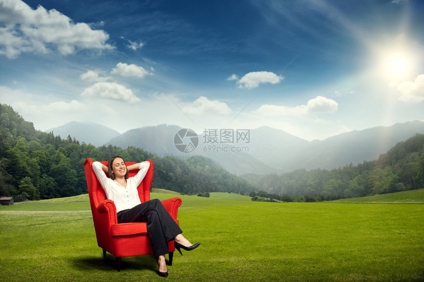 坐在绿草地上的红椅子上与山丘森林和天空相伴的图片