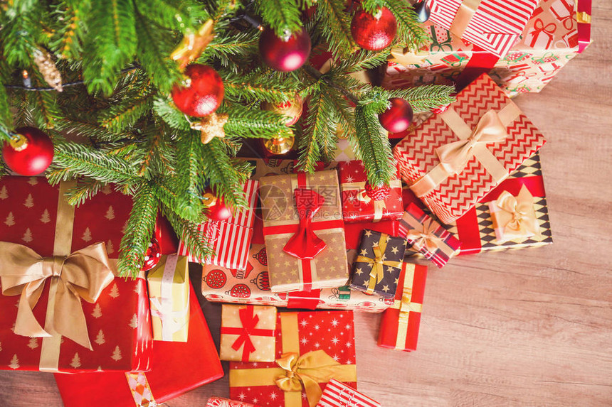 圣诞树枝的顶视图组成与一堆不同的礼物在五颜六色的节日包装上系着蝴蝶结木地板上云杉树下的一堆礼物背图片