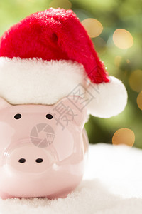 粉红小猪银行在雪花上穿红色和白色圣塔帽图片