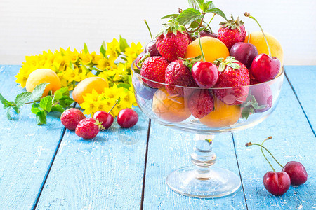 草莓樱桃古代花瓶中的杏仁和蓝桌上的浆果及花朵图片