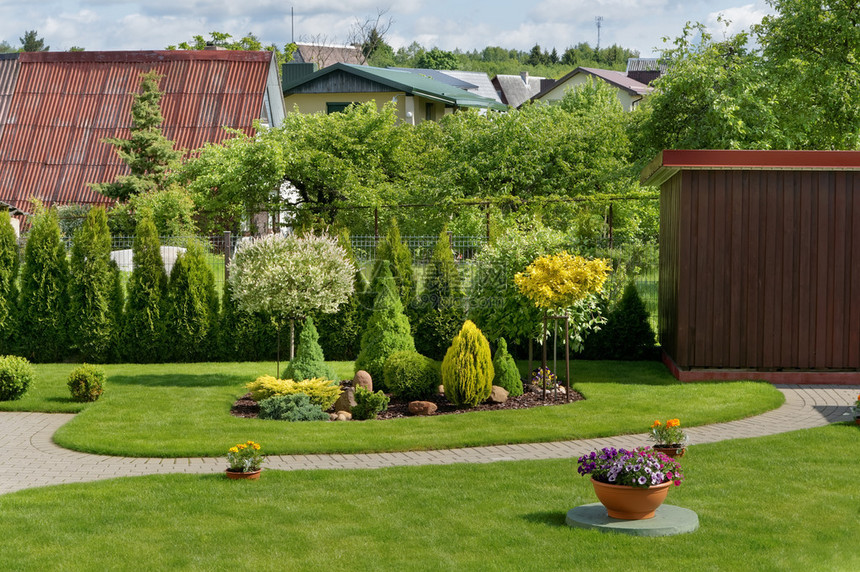 拥有绿色草坪鲜花和灌木林的欧洲装饰理想农村花园的一部分图片