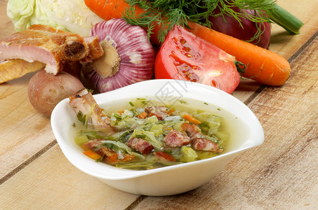 白碗美食蔬菜汤和木制背景上的熏排骨卷心菜西红柿葱韭菜胡萝卜大蒜图片