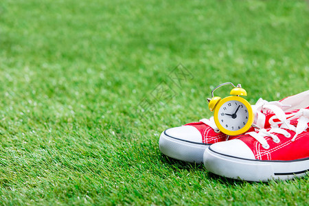 绿草背景上的红色运动鞋和黄色闹钟图片