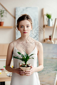 拥有绿色陶植物并观看相机的美丽年轻女艺图片