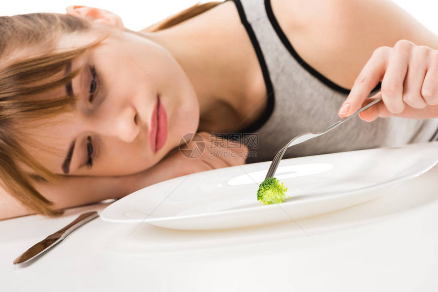 忧郁的瘦女人吃一块西兰花椰菜从板盘图片