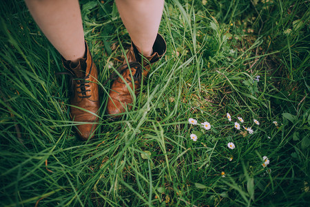 年轻女子的腿穿着棕色皮短靴在绿色草地图片