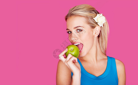 美丽的金发年轻美女咬进新鲜的绿苹果里看着镜头的侧面粉红图片