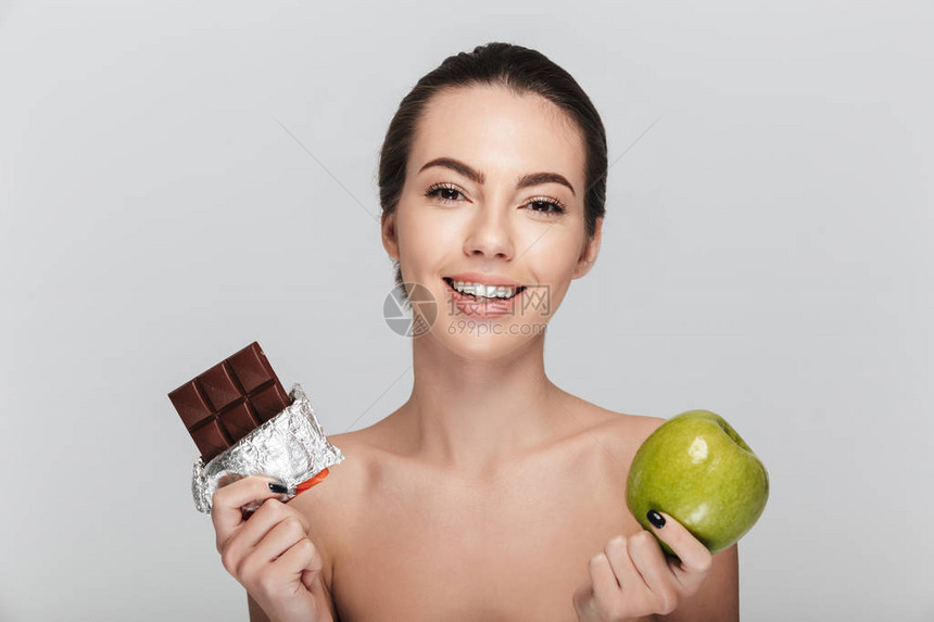 快乐的年轻女人在苹果和巧克力之间做出选择图片