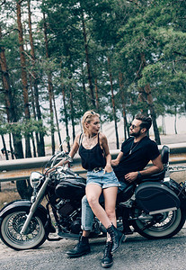 在绿林附近路上互相看着对方双骑着黑色摩托车的图片