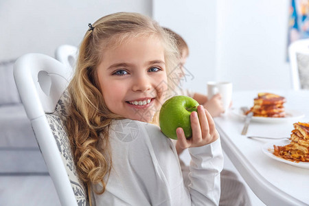 有绿苹果的可爱小孩在和家人一起吃早饭时看图片