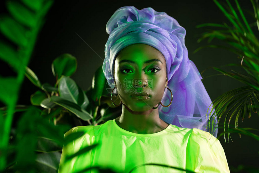 传统铁丝头围在绿色照下观看相机的年轻非洲女图片