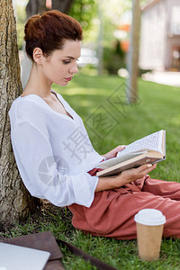 坐在公园树干上看书的年轻女子的侧面图片