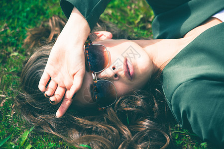 带着太阳眼镜的城市年轻女子躺在草地上图片