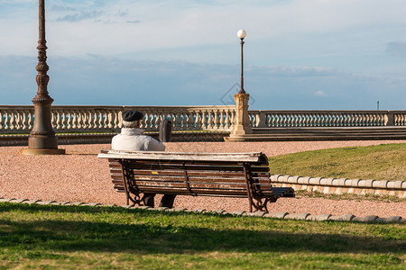孤单的老人坐在露天广场附近的公共长椅上图片
