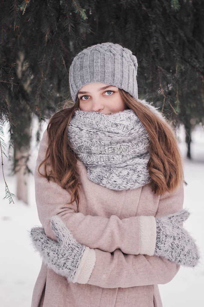 一个年轻女孩在寒冷的冬日站在森林里的垂直肖像寒冷的冬天气戴着针织帽羊毛围巾和手套的少年在松树图片