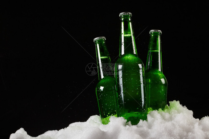 黑色背景中雪地里的啤酒瓶图片
