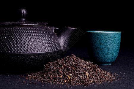 黑茶壶与健康茶叶隔离在黑色高清图片