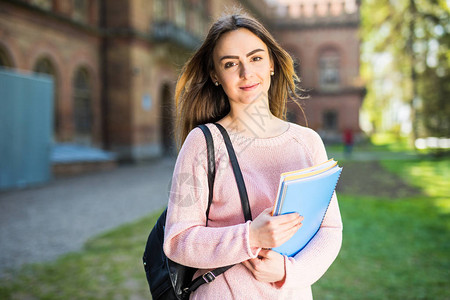 大学生女孩在校园公微笑着书本或笔记本图片