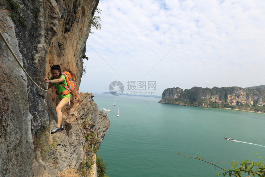 在海边山崖上攀登的年轻女子攀岩者图片