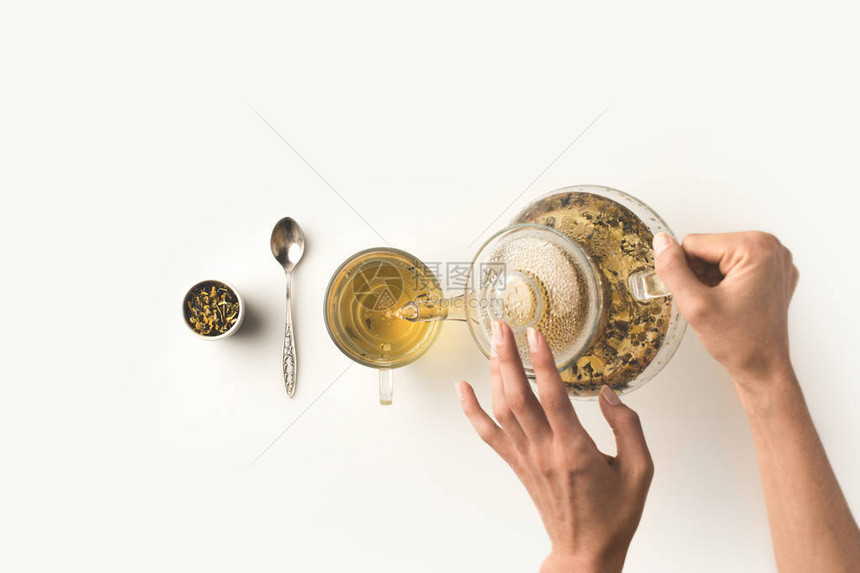将新鲜有机草药茶从水壶倒入白玻璃的图片