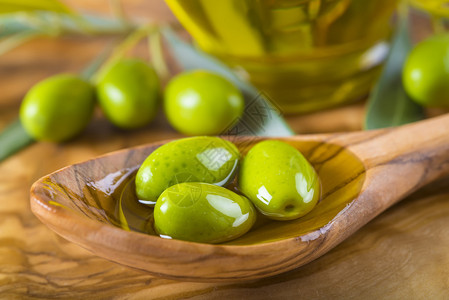 木勺上的绿橄榄和初榨橄榄油图片