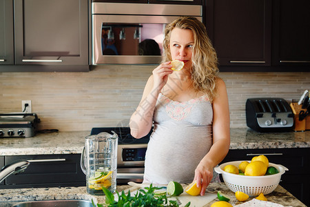白种金发孕妇吃柑橘柠檬汁的肖像站在家里的厨房里看着别处图片
