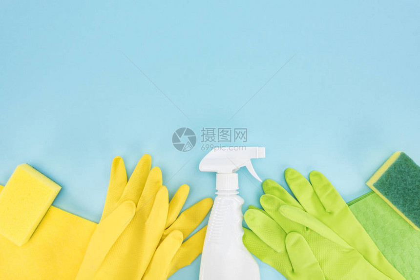 黄色和绿色橡胶手套海绵抹布和喷雾瓶及含清洁剂的蓝色背景图片