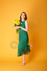 身着绿裙子的年轻美女带着黄春郁金香花束在图片
