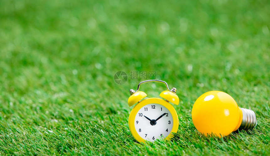 绿色草地背景的黄色闹钟和黄色灯泡图片