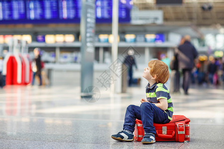 坐在机场行李箱上的小累可爱男孩带着大手提箱等待着的悲哀儿童图片