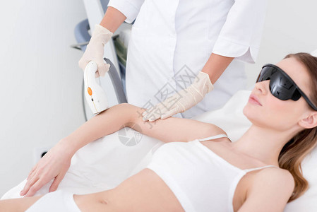 接受美容师在美容院做手臂激光除毛手术的妇女图片
