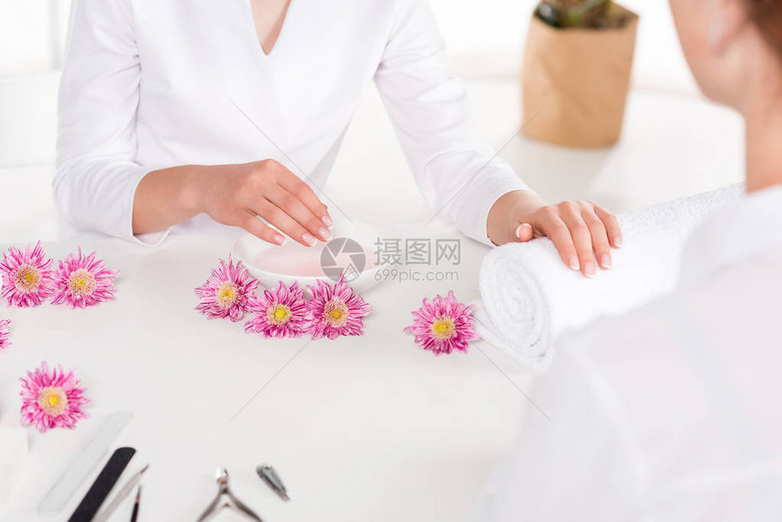 美甲师和女在美容院用鲜花指甲钳指甲锉和角质层推杆在餐桌上接受指甲图片