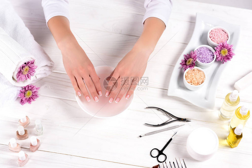 女在餐桌上用鲜花毛巾五颜六色的海盐芳香油瓶指甲油奶油容器和美容沙龙修指甲工具接受图片