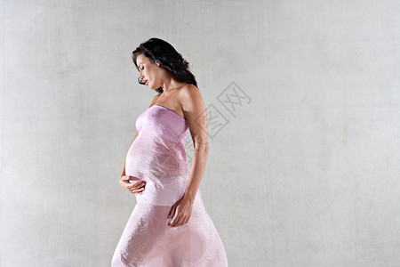 围着粉红色丝绸浮织物的孕妇身躯侧面图片