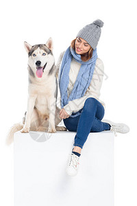 哈士奇狗和戴针织帽和围巾的女人坐在白色立方体上图片