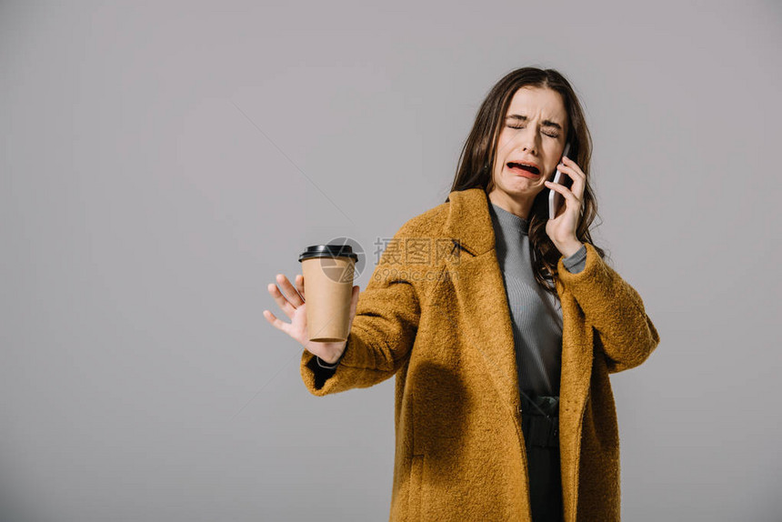 穿着米花大衣的哭泣女孩拿着咖啡去谈智能手机图片