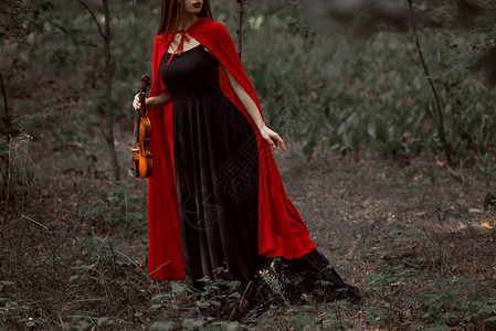 穿着黑裙子和红斗篷的优雅神秘女人在森林里拉着图片
