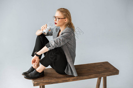 坐在以灰色隔离的木板凳上喝着玻璃牛奶时图片