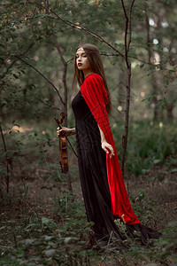 穿着黑裙子和红斗篷的迷人神秘女人在森林背景图片