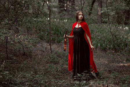 穿着黑裙子和红斗篷的美丽神秘女孩在森林图片