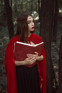穿着红色斗篷和花圈的美丽神秘女孩在森林背景图片