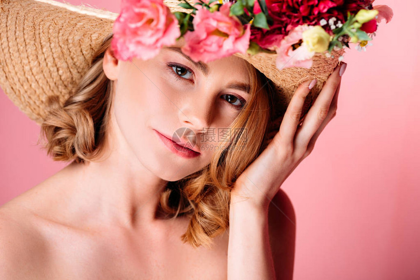 带着鲜花戴着帽子的年轻美女看着粉红色图片