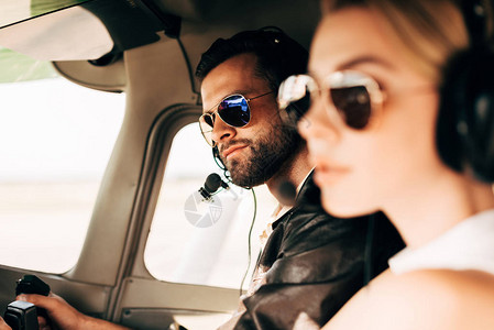 英俊的男飞行员在头盔和太阳镜中与女友坐在飞机舱里时选择图片