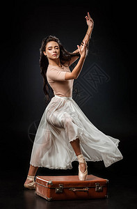 穿着白裙子的漂亮芭蕾舞女郎站在黑暗背景的图片