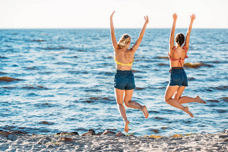年轻女在沙滩上举手跳跃的背影图片
