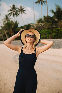 迷人的女人在沙滩上戴着帽子太阳镜和连衣裙图片