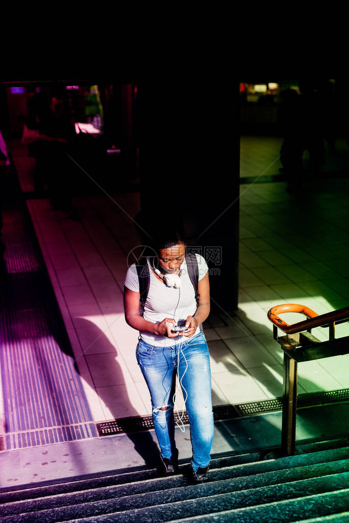 使用智能手机持从地下走上楼的年轻黑人美女图片
