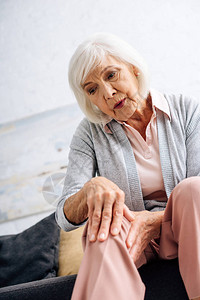 高龄妇女膝关节炎和坐在公寓沙发上图片